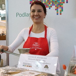 Stoisko Podlaskiego Centrum Produktu Lokalnego - zbliżenie na Panią Annę Gąsowską prezentującą promienny uśmiech. W tle podlaskie logo żubra.